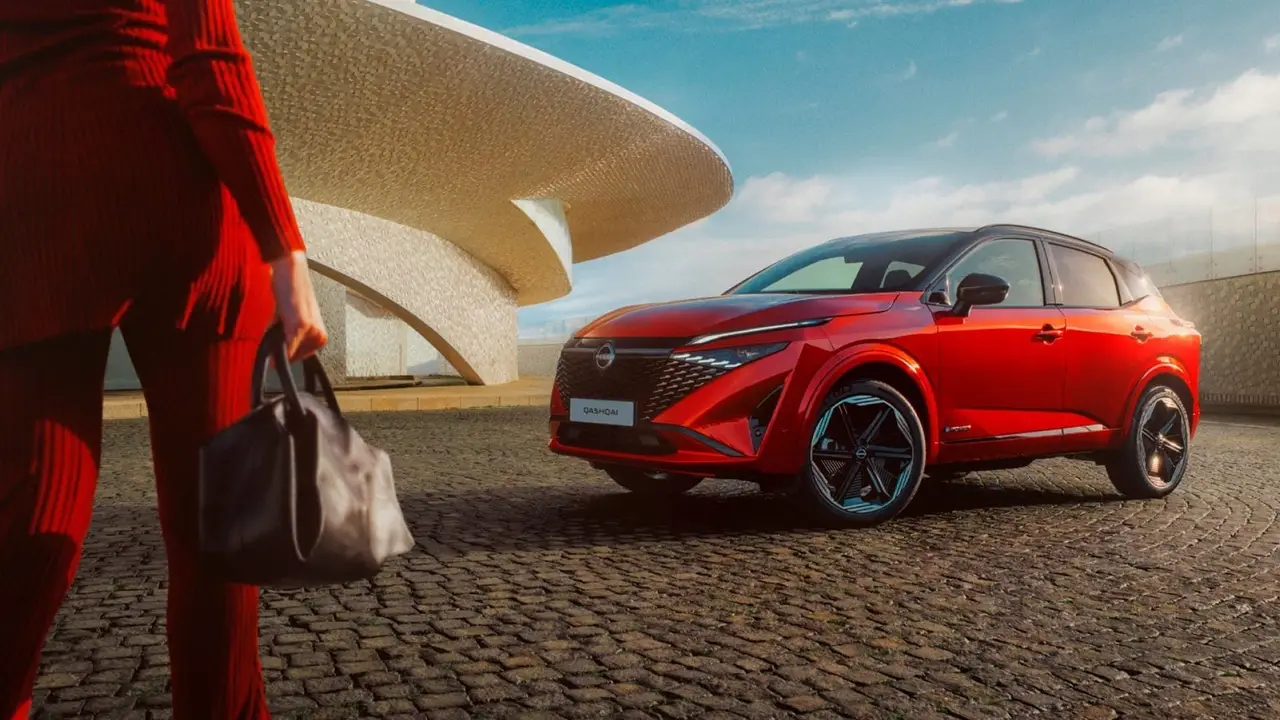 in roter Nissan Qashqai steht auf einem Platz mit moderner Architektur im Hintergrund.