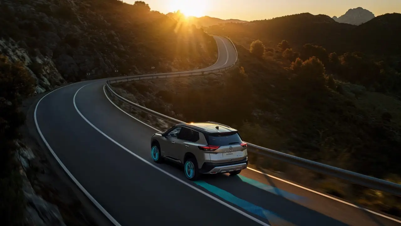 Ein Nissan X-Trail fährt bei Sonnenuntergang durch eine kurvenreiche Bergstraße.