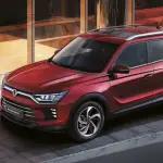 Roter KGM Korando SUV vor moderner Glasfassade bei Abendlicht.