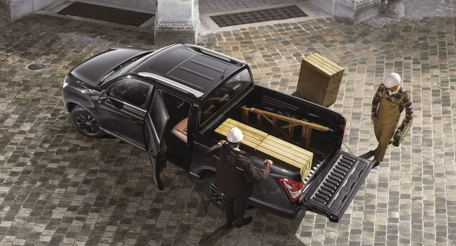 KGM Musso Grand mit geöffneter Ladefläche beim Beladen durch Bauarbeiter