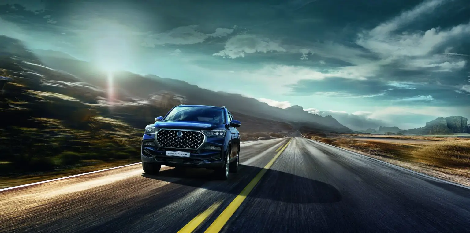 KGM Rexton fährt bei Sonnenuntergang auf offener Straße durch eindrucksvolle Berglandschaft.