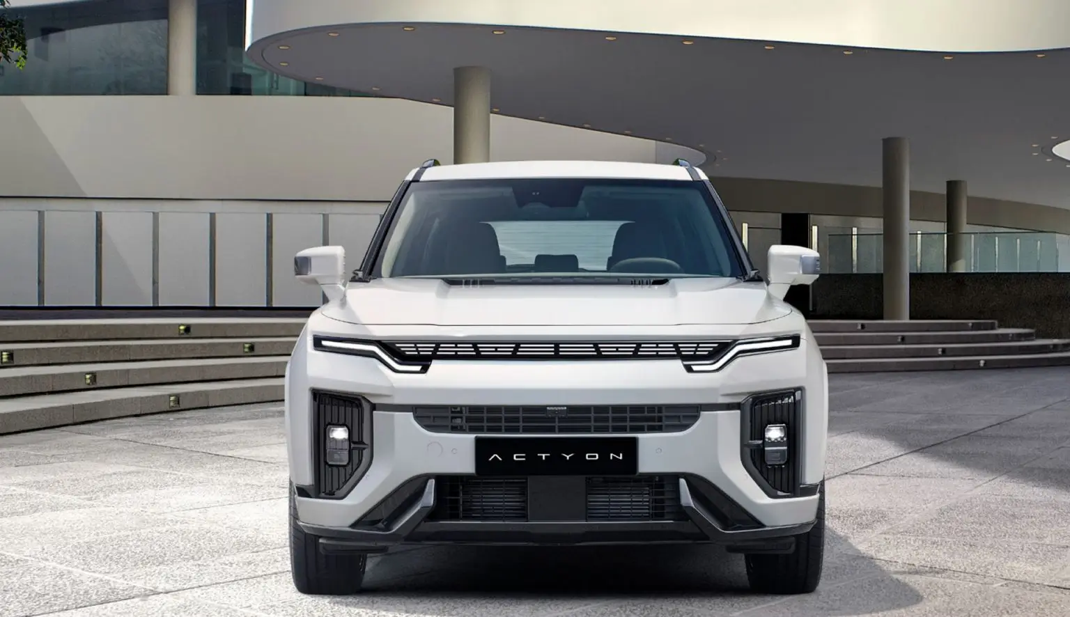 Frontansicht eines weißen KGM Actyon SUV vor modernem Gebäude.