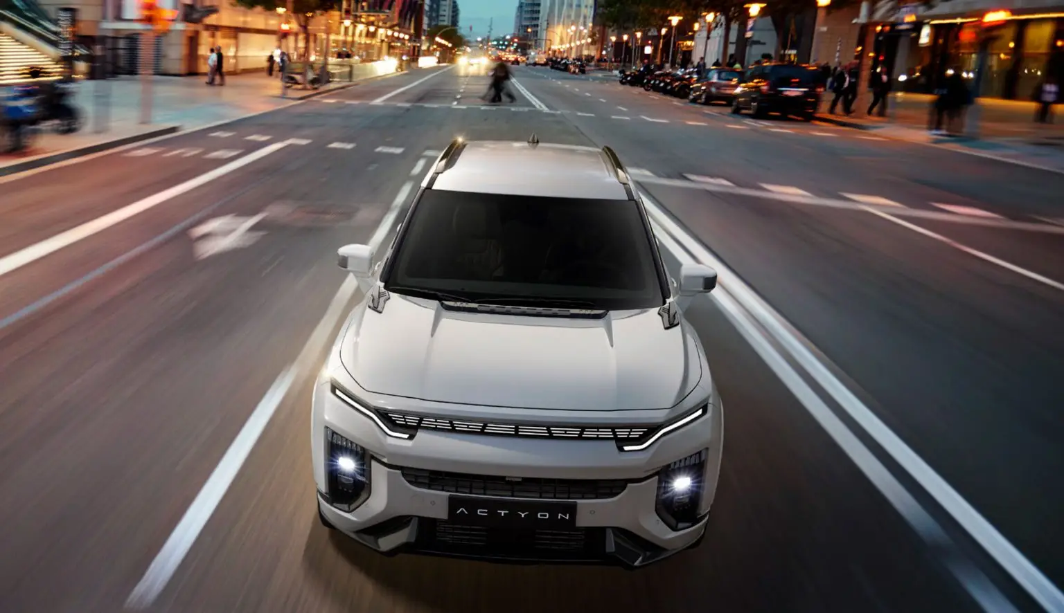 Der KGM Actyon fährt bei Dämmerung durch eine beleuchtete Innenstadt.