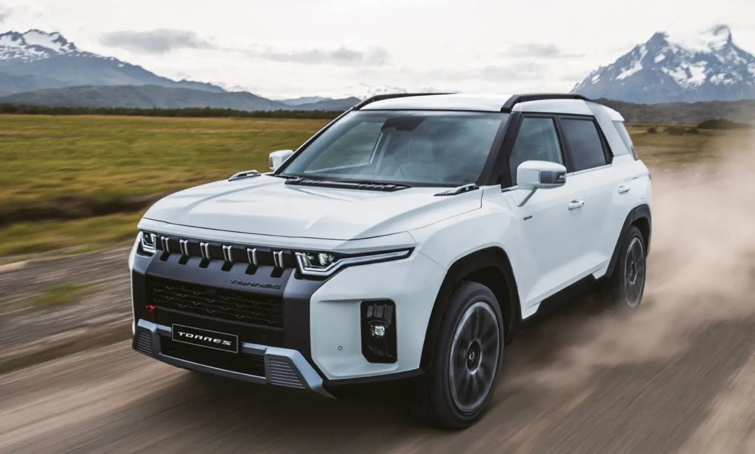 Ein weißer KGM Torres SUV fährt auf einer staubigen Schotterstraße mit Bergen im Hintergrund.