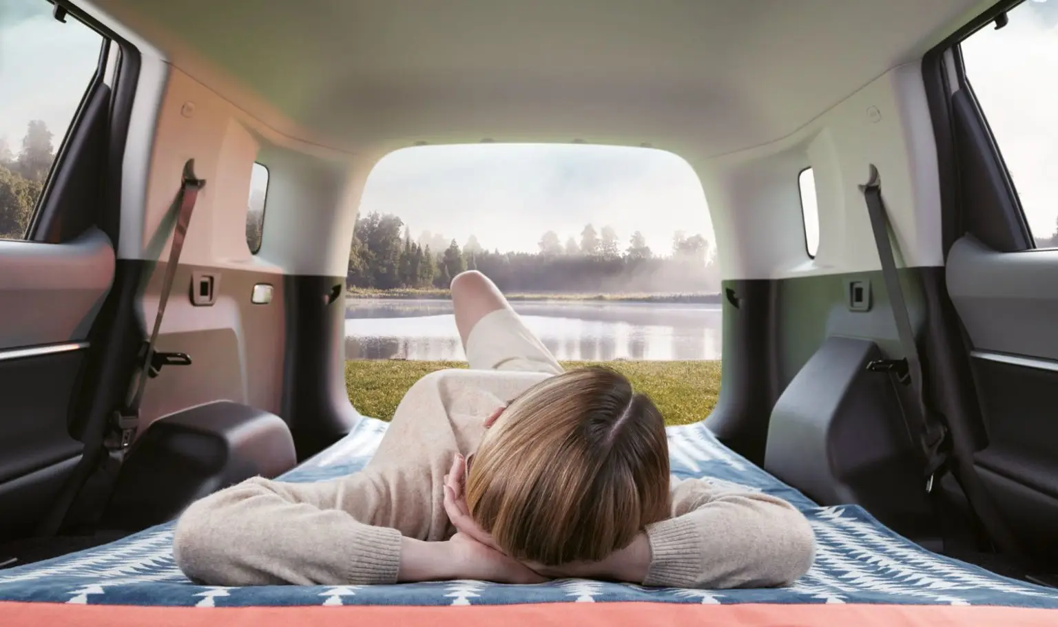Frau liegt entspannt im umgeklappten Kofferraum des KGM Torres und blickt durch die geöffnete Heckklappe auf einen See.
