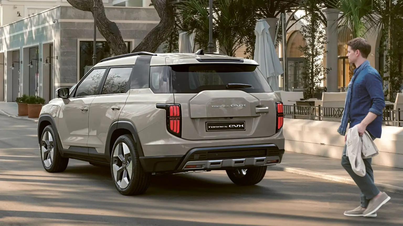 Der vollelektrische SUV KGM Torres EVX steht geparkt vor einem Straßencafé, ein Mann nähert sich dem Fahrzeug.