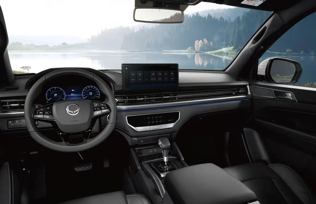 Digitales Cockpit und Infotainment im KGM Musso mit Blick auf die Seelandschaft.